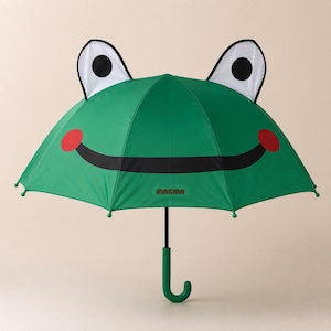 Puede incluir: Paraguas verde con forma de rana con una boca negra sonriente, círculos rojos para las mejillas y ojos blancos y negros. El paraguas tiene un mango verde curvado y el nombre de la marca "macma" impreso.