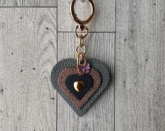 May include: A gray, pink, and blue layered heart-shaped keychain with a gold-colored metal ring and a small butterfly charm.