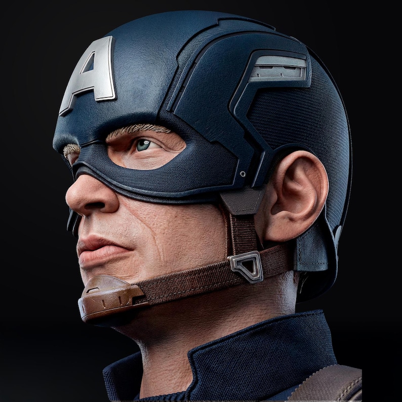 Op de afbeelding: Een gedetailleerd zijaanzicht van een Captain America-helm. De helm is voornamelijk marineblauw met een zilveren "A" op het voorhoofd. Het masker bedekt de ogen en er is een bruine kinriem zichtbaar. De achtergrond is zwart.