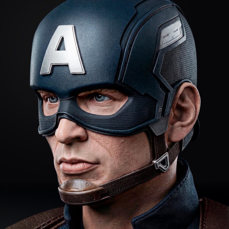 Op de afbeelding: Een gedetailleerde close-up van een Captain America-helm. De helm is voornamelijk marineblauw met een grote zilveren "A" op het voorhoofd. Het masker en de kinband zijn bruin. Het gezicht van het personage is zichtbaar, met blauwe ogen en een vastberaden uitdrukking.