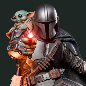 May include: A detailed statue of The Mandalorian holding a blaster with a red light, with Grogu, also known as Baby Yoda, peeking over his shoulder. The Mandalorian wears a silver helmet and armor, with a dark cape. Grogu is wrapped in a tan cloth.