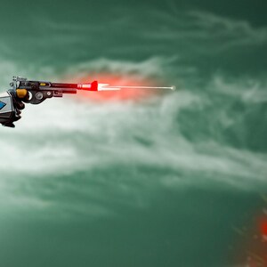 May include: A futuristic ray gun with a red laser beam firing from the barrel. The gun is held by a gloved hand against a cloudy, green background. The gun has a black, silver, and yellow design.