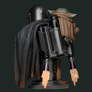 May include: A detailed statue of The Mandalorian with Grogu. The Mandalorian is in a black helmet and armor, with a dark cape. Grogu is wrapped in a brown blanket. The statue has a jetpack with orange flame effects.