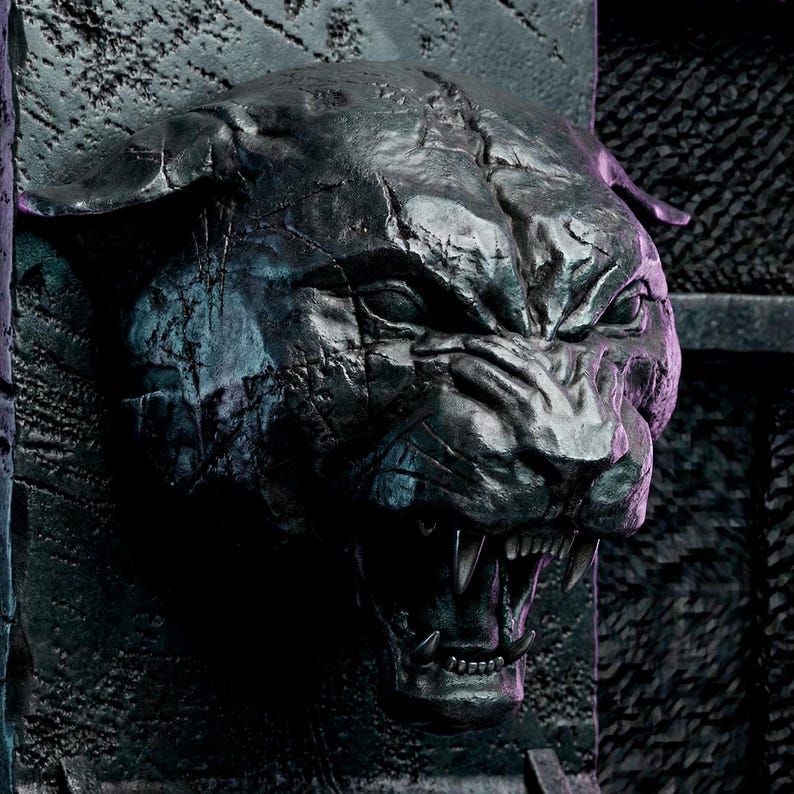 Pu&ograve; includere: Scultura scura di una testa di pantera che ringhia. La bocca della pantera &egrave; aperta, rivelando denti affilati. La scultura ha una superficie strutturata ed &egrave; montata su uno sfondo scuro e strutturato.