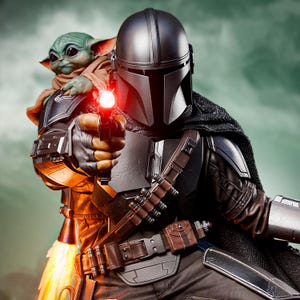 May include: A detailed action figure of The Mandalorian holding a blaster, with Grogu (Baby Yoda) in tow. The figure is clad in dark armor with a helmet, and Grogu is wrapped in a brown cloak. The blaster emits a red light.