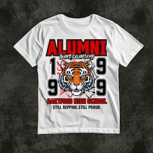 May include: A white short-sleeve t-shirt featuring a graphic of a tiger face centred between the numbers 19 and 99. The text reads ALUMNI, TWENTY SEVEN YEARS, OAKWOOD HIGH SCHOOL, and STILL REPPING. STILL PROUD. in red and black lettering.