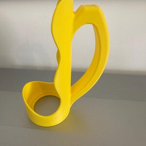 May include: A bright yellow, abstract-shaped object with a circular base and a curved handle. The design features smooth, rounded edges and a hollow center. The object appears to be made of a solid material, possibly plastic or resin.