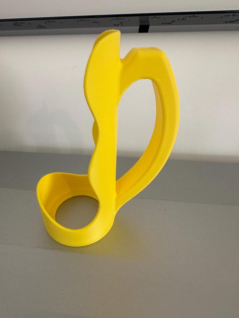 May include: A bright yellow, abstract-shaped object with a circular base and a curved handle. The design features smooth, rounded edges and a hollow center. The object appears to be made of a solid material, possibly plastic or resin.