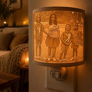 May include: A night light with a personalized image of four people. The lamp has a warm, glowing light and is plugged into a wall outlet. The image is a sepia-toned photograph of four people standing outside.