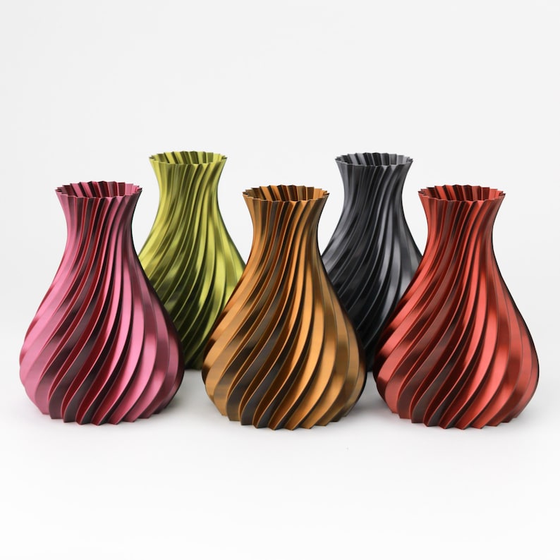 May include: A collection of five vases with a spiraling, ribbed texture. The vases are finished in metallic shades of magenta, lime green, bronze, black, and red. Each vase features a flared rim and a rounded, bulbous body shape.