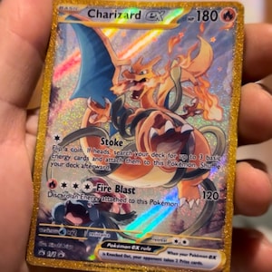 Peut inclure: Une carte à collectionner Pokémon Charizard EX avec une bordure dorée. La carte présente une illustration vibrante de Charizard dans des tons orange, rouge et bleu. Le texte sur la carte comprend "Charizard EX", "Stoke" et "Fire Blast".