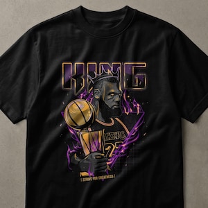 Puede incluir: Camiseta negra con un gráfico de un jugador de baloncesto sosteniendo un trofeo y un balón de baloncesto. La palabra "KING" está encima de la cabeza del jugador, con el texto "LAKERS 23" en la camiseta. La frase "STRIVE FOR GREATNESS" está en la parte inferior.