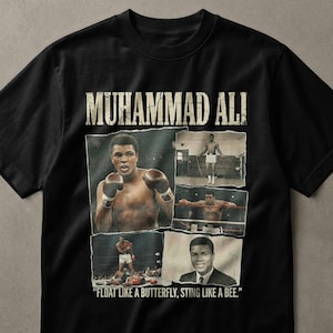 May include: Black t-shirt featuring a collage of images of Muhammad Ali. The shirt includes the text "MUHAMMAD ALI" at the top and the quote "FLOAT LIKE A BUTTERFLY, STING LIKE A BEE." at the bottom. The images show Ali boxing and training.