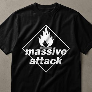May include: A black short-sleeved t-shirt featuring a white graphic print on the chest. The design consists of a white diamond outline containing a white flame icon above the text "massive attack" written in a bold, lowercase sans-serif font.