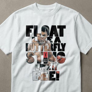 以下が含まれることがあります： グラフィックデザインが施された白いTシャツ。「FLOAT LIKE A BUTTERFLY STING LIKE A BEE！」の文字が重ねられたフォントでデザインされています。「STING」の文字にはボクシンググローブのグラフィックが施されています。「ALI」の文字も確認できます。