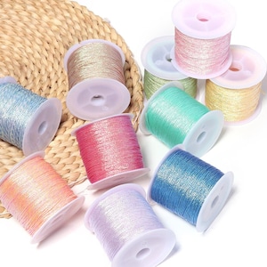 May include: A collection of ten small plastic spools wrapped in metallic, shimmering embroidery thread in various colors including pink, blue, green, gold, peach, and lavender. The spools are arranged in a cluster, showcasing a glossy finish.