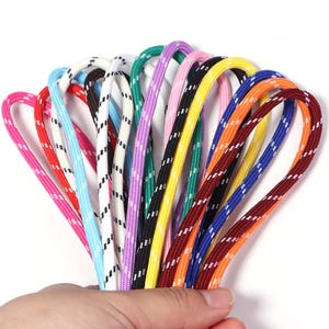 May include: A collection of multi-colored braided cords featuring a woven texture and a repeating white diagonal dash pattern. The assortment includes vibrant shades of pink, red, light blue, white, green, purple, black, yellow, orange, and maroon.