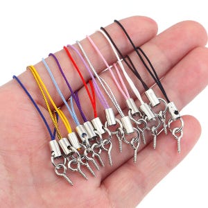 May include: A collection of multi-coloured lanyard straps featuring thin nylon cords in blue, yellow, light blue, purple, red, lavender, silver, pink, white, and black. Each cord is attached to a silver-toned metal crimp and a small screw eye hook.