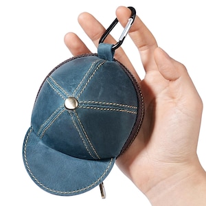 Könnte beinhalten: Eine blaue Leder-Geldbörse in Form einer Baseballkappe mit gebogenem Schirm und Knopf oben. Die Geldbörse hat einen braunen Reißverschluss und ist an einem schwarzen Karabinerhaken befestigt.