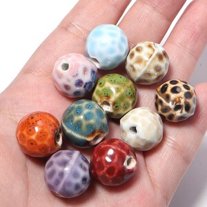 Puede incluir: Una colección de diez cuentas esféricas de cerámica con un acabado de esmalte brillante y agrietado en varios colores, incluyendo azul claro, rosa, verde, naranja, morado, rojo, blanco y marrón, cada una con un orificio central.