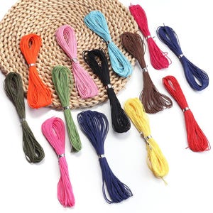 May include: A collection of twelve individual hanks of thin, multi-colored cord, each secured with a small silver-toned metal band. The colors include orange, pink, light blue, brown, dark red, navy blue, olive green, black, yellow, and bright red.