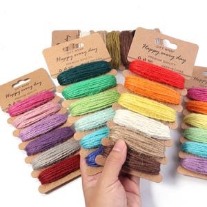 May include: A collection of multi-coloured jute twine spools wrapped on brown cardboard cards. Each card features the text "GIFT WRAP Happy every day PREMIUM QUALITY MADE IN CHINA". The twine comes in various colours including red, green, blue, yellow, and pink.