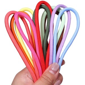 Könnte beinhalten: Eine Sammlung mehrerer geflochtener Kordeln in verschiedenen Farben, darunter Rot, Orange, Gelb, Pink, Olivgrün, Hellgrün, Braun, Lavendel und Hellblau. Jede Kordel ist geschlungen und weist eine texturierte, gewebte Oberfläche auf.
