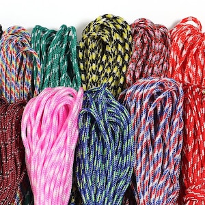 May include: A collection of coiled nylon paracord bundles in various colours including solid pink, bright green, yellow and black, red and white, blue and white, and multi-coloured patterns. Each bundle consists of tightly woven synthetic rope.