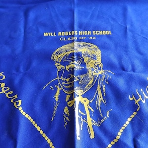 以下が含まれることがあります： 青色の布地に、ウィル・ロジャースの金色のイラストと「Will Rogers High School Class of '42」の文字が描かれています。デザインにはロープのような縁取りと筆記体の文字が含まれています。