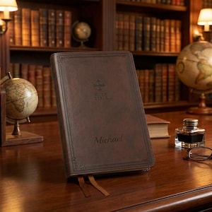 May include: A brown leather Bible with the name "Michael" embossed on the cover, resting on a wooden desk. The desk is surrounded by bookshelves filled with books and globes, creating a classic library setting.