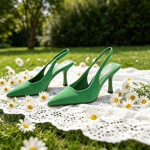 Puede incluir: Un par de zapatos de tacón verde brillante con punta y correa trasera. Los zapatos tienen correas finas y tacones de aguja. Se colocan sobre un paño de encaje blanco con margaritas.