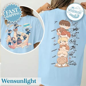 May include: Light blue t-shirt featuring a cartoon illustration of a boat with cartoon characters and the word "SWIM". The back of the shirt displays cartoon characters, signatures, and names. The brand name "Wensunlight" is at the bottom.