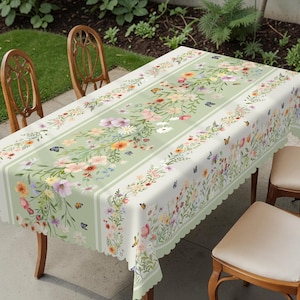 May include: A rectangular tablecloth with a floral and butterfly design. The tablecloth has a light green center with a floral pattern and white stripes. The edges are scalloped. The flowers are in shades of pink, yellow, and orange.