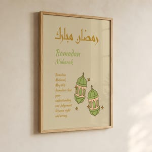 Può includere: Una stampa artistica da parete incorniciata con sfondo beige, il testo arabo Ramadan Mubarak in oro, il testo inglese Ramadan Mubarak in verde e una citazione sul Ramadan. Sono illustrate due lanterne verdi e rosa con stelle dorate.