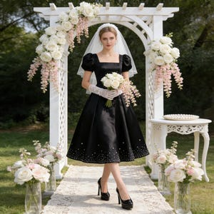 May include: A black satin dress with a square neckline and puff sleeves. The dress features a beaded hemline and is paired with black platform heels. The person is holding a white bouquet and wearing a veil and lace gloves. The setting is an outdoor wedding.