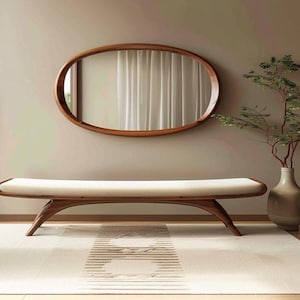 May include: A contemporary interior scene with a wooden oval mirror, a bench with a cream cushion, and a vase with greenery. The room has a neutral colour palette with a light-coloured rug.
