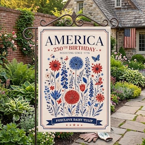 Könnte beinhalten: Eine Gartenflagge mit dem Text "AMERICA 250th BIRTHDAY" und floralen Illustrationen in Rot, Weiß und Blau. Die Flagge enthält die Worte "RESISTING SINCE 1776" und "FOXCLOVE DAISY TULIP". Die Flagge wird auf einem Metallständer in einem Garten gezeigt.