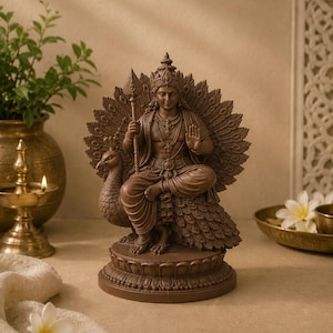 May include: A brown statue of a deity seated on a peacock, holding a spear. The statue has intricate details, including a crown and jewelry. The peacock's feathers form a backdrop. The statue is on a round base.