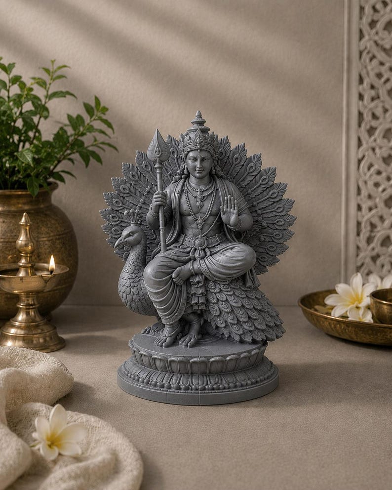 May include: A gray statue of a deity seated on a peacock, holding a spear. The statue features intricate details, including a crown, jewelry, and a detailed peacock feather backdrop. The statue is on a round base.