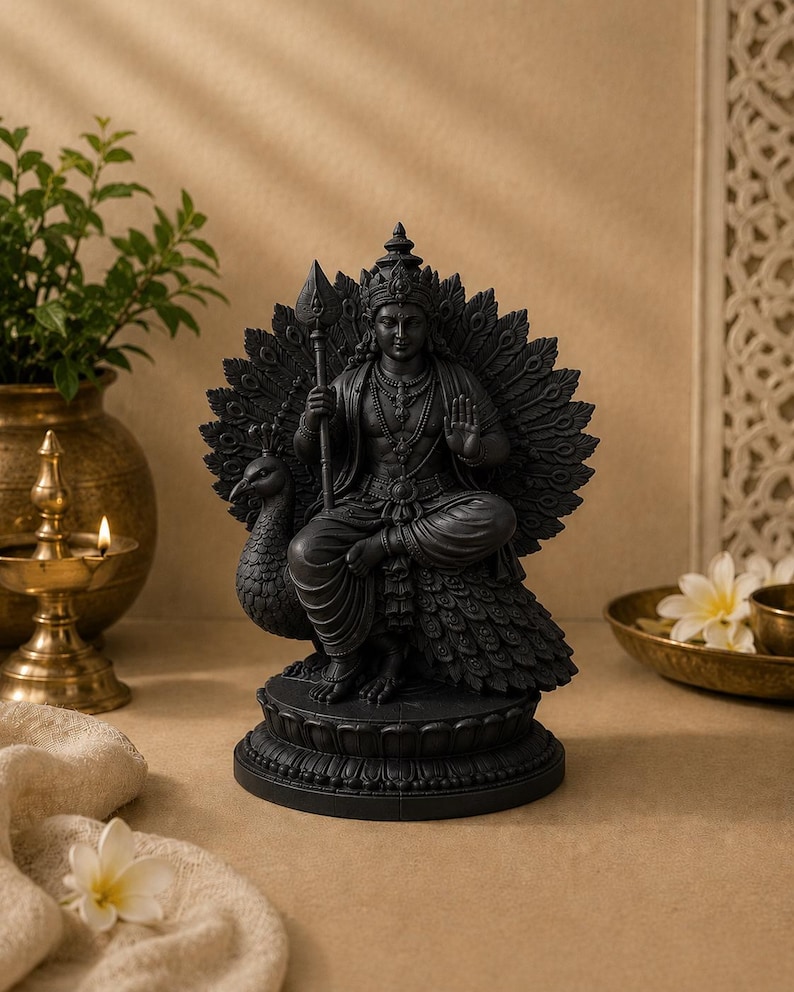 May include: A black statue of a deity seated on a peacock, holding a spear. The statue has intricate details, including a crown and jewelry. The peacock's feathers are fanned out behind the deity. The statue is on a decorative base.