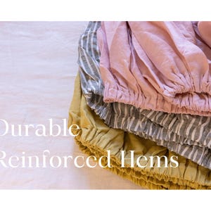 May include: A close-up of folded fabric in pink, grey and yellow, with gathered hems. The image includes the text "Durable Reinforced Hems". The fabrics are stacked on top of each other.