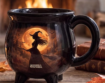 May include: A black ceramic cauldron-shaped mug featuring a printed illustration of a witch on a broomstick against a large orange full moon. The name SOPHIA is printed in white lettering near the base of the witch's dress. The mug has three feet.