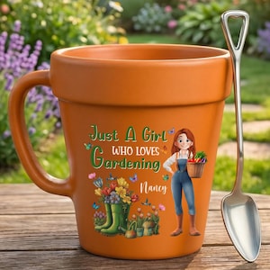 May include: A terracotta-colored ceramic mug shaped like a flower pot, featuring a graphic of a person, flowers, and the text "Just A Girl WHO LOVES Gardening Nancy". A silver-toned metal spoon with a shovel-shaped handle rests beside the mug.