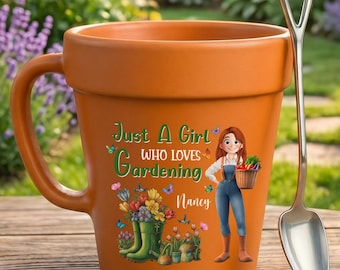 May include: A terracotta-colored ceramic mug shaped like a flower pot, featuring a graphic of a person, flowers, and the text "Just A Girl WHO LOVES Gardening Nancy". A silver-toned metal spoon with a shovel-shaped handle rests beside the mug.
