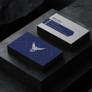 May include: Two stacks of rectangular business cards. One stack shows a dark blue background with a white phoenix logo and purple geometric lines. The other stack displays white cards with a dark blue banner containing the text Ethan Parker, Creative Director, (415) 555-0138, ethan.parker@example.com, and 742 Market Street, San Francisco, CA 94102.