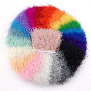 May include: A circular arrangement of colourful feather trim in a rainbow spectrum. The colours include pink, white, grey, black, blue, green, yellow, orange, and purple. A section of pink feather trim is attached to a white strip.