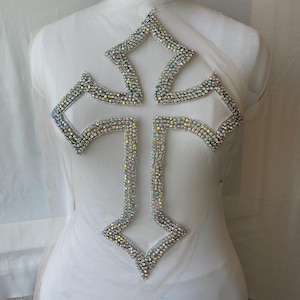 Peut inclure: Grand appliqué en forme de croix étincelante, ornée de strass irisés. La croix est bordée d'argent et posée sur un tissu blanc transparent. Cette applique décorative convient aux vêtements ou aux projets d'artisanat.