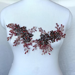 May include: A pair of symmetrical floral-shaped appliqués crafted from deep red and dark burgundy crystals, beads, and faceted glass stones. The design features intricate wire-wrapped branches extending outward with dangling teardrop-shaped beads.