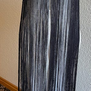 May include: A strapless black garment featuring a dense layer of long, thin vertical fringe that hangs from the top edge. The fringe covers the entire front surface, creating a uniform, linear texture that extends downwards in straight, parallel lines.