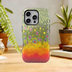 May include: A smartphone case featuring a colorful design inspired by a brown trout. The case has a black border and a pattern of red, yellow, and blue spots over a green and yellow background, resembling fish scales.